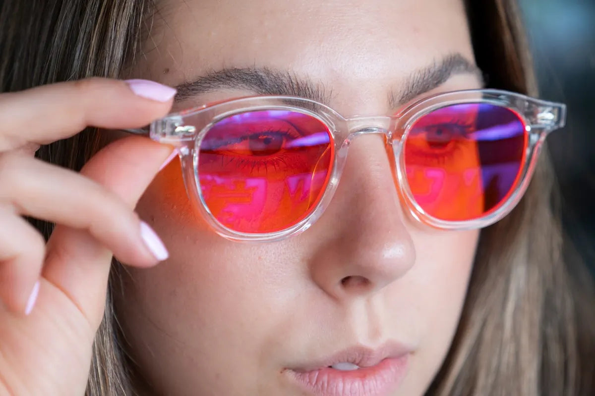 Mujer acomodándose unos lentes Sleep Mode de Insae, de armazón transparente y mica roja
